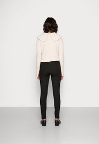 Jasnobeżowy prążkowany sweter z szerokim kołnierzem w połączeniu z czarnymi dopasowanymi legginsami. Strój charakteryzuje się długimi rękawami i czarnymi płaskimi butami.