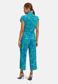 Combinaison à motifs floraux bleus et verts avec une taille ajustée et des manches courtes, présentant des jambes larges et une texture de tissu lisse.