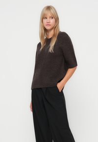 Brown textured short-sleeve sweater with a relaxed fit, paired with loose black trousers, showcasing a casual and comfortable style.