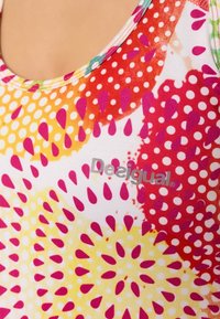 Närbild av en färgglad ärmlös topp med cirkulära mönster i röd, gul och rosa, med märket "Desigual" på tyget.