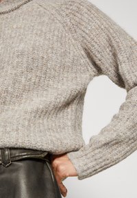 Jasnoszary sweter z dzianiny o prążkowanej fakturze i długimi rękawami, charakteryzujący się luźnym krojem. Stylizowany z ciemną spódnicą z paskiem.