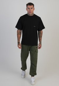 Svart bomullströja med korta ärmar och en liten logotyp, kombinerad med olivgröna cargobyxor med fickor och elastiska muddar. Vita sneakers.