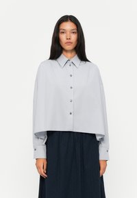 Hellgrau gefüttertes Button-Up-Hemd mit klassischem Kragen, übergro�ßen Ärmeln und silbernen Knöpfen, kombiniert mit einem dunklen, plissierten Midirock.