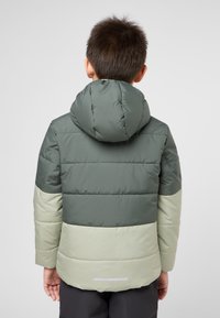 Giacca imbottita con cappuccio in blocchi di colore verde scuro e verde chiaro, con un tessuto trapuntato e un accento riflettente sul retro.