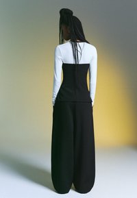 Fekete-fehér hosszú ujjú felső, testhezálló nyakkivágással és laza fekete nadrággal. Jellemzője a sima textúra, az igényes kialakítás és a minimalista stílus.