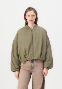 Olijfgroene bomberjack met een ritssluiting aan de voorkant, een losse pasvorm en volumineuze mouwen. Draag het over lichtbruine jeans met een vervaagd ontwerp.