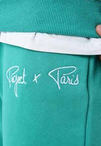 Sudadera en color azul verdoso con textura acanalada y ribete blanco, con "Project x Paris" bordado en letras blancas en la parte delantera.