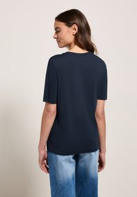 T-shirt bleu marine à manches courtes avec un col rond, texture lisse et coupe décontractée, assorti à un jean en denim dégradé bleu clair.