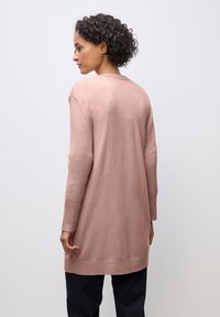 Lång, mjuk cardigan i ljusrosa, med ribbade manschetter och fåll. Designen har en avslappnad passform och är gjord av lätt stickad material.