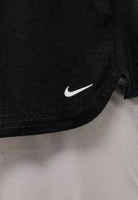 Μαύρο αθλητικό ύφασμα με μικρές διατρήσεις και λευκό λογότυπο Nike swoosh κοντά στην άκρη του τελειώματος.