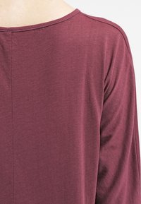 Long-sleeve top in a deep burgundy fabric, featuring a round neckline and a smooth texture with subtle stitching details.