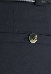 Marineblaue Stoffhosen mit glatter Textur, ausgestattet mit einem dunklen Knopf im Four-Hole-Design und subtilen Musterelementen.