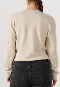 Beige gebreide trui met lange mouwen en geribbelde manchetten, gecombineerd met donkergrijze jeans met twee achterzakken.