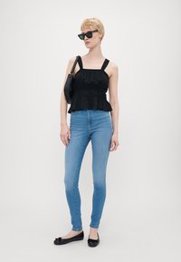 Svart, volang peplum topp med vide stropper, paret med lyseblå skinny jeans og flate svarte sko. Modell med kantete svarte solbriller.