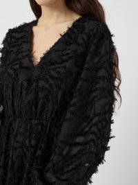 Black long-sleeve dress featuring a textured, frayed design with a deep V-neckline and flowing silhouette. Lightweight fabric.
