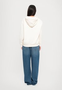 Crème-kleurige capuchontrui met een relaxte pasvorm, gecombineerd met brede blauwe denim jeans met subtiele stiksels en achterzakken.