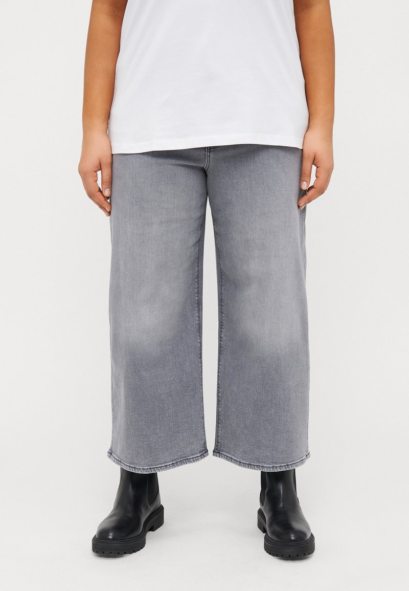 Wide-leg grey denim trousers with a faded finish, featuring a raw hem. Paired with black ankle boots and a plain white t-shirt.