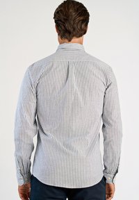 Κλασικό πουκάμισο μακρυμάνικο σε ανοιχτό γκρι με λεπτές κάθετες λευκές ρίγες. Διαθέτει γιακά με κουμπιά και μανίκια με μανσέτες και κουμπιά.