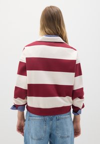 Felpa a righe bordeaux e crema con colletto, caratterizzata da un design corto e maniche arrotolate che rivelano un motivo a quadri blu sottostante.