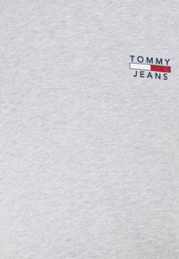 Šedé bavlněné tričko s malou vyšívanou logem "TOMMY JEANS" v modré a červené barvě na levé oblasti hrudi. Měkká, hladká textura.