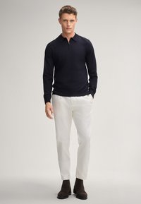 Herren Pullover mit langen Ärmeln in Navy mit Reißverschlusskragen, kombiniert mit cremefarbenen Hosen und dunkelbraunen Knöchelboots. Glatte Textur, schmal geschnittenes Design.