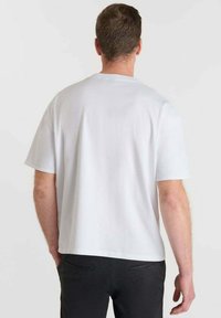 T-shirt bianco in cotone con scollo rotondo, maniche corte e vestibilità rilassata. Texture liscia, senza motivi, abbinato a pantaloni scuri.