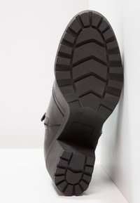 Botte en cuir noir avec semelle texturée, présentant un motif strié et une base solide et plate. Bretelle latérale avec détail de boucle visible. Taille 37.