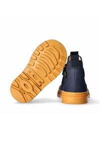 Stivale della marina con suola in gomma color tawny caratterizzato da un motivo di battistrada. Il dettaglio posteriore mostra un anello in tessuto e un occhiello in metallo per la chiusura.