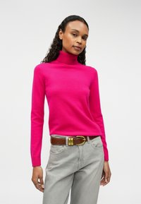 Fuchsia turtleneck sweater, knit fabric, ribbed cuffs, paired with gray pants and a brown belt featuring a gold buckle.