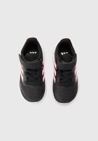 Baskets de sport noires avec des rayures roses, une sangle Velcro et une tige en mesh texturé. Bout arrondi et semelle blanche rembourrée.