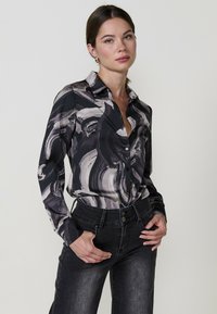 Camicia a maniche lunghe nera con motivi astratti grigi e bianchi; vestibilità comoda; abbinata a jeans grigi scuri in stile classico.