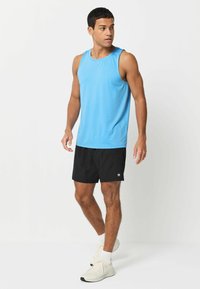 Jasnoniebieski sportowy top bez rękawów, czarne szorty i białe sneakersy. Top ma okrągły dekolt; materiał wydaje się oddychający o gładkiej teksturze.