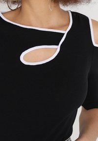 Top negro con ribetes blancos, con un recorte único en el hombro y mangas de tres cuartos. Textura suave y diseño ajustado.