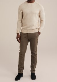 Světlý béžový pletený svetr s žebrovanými manžetami a lemem, doplněný olivově zelenými kalhotami na tělo a černými semišovými kotníkovými botami.