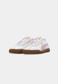 Baskets blanches et beige avec des accents roses, bout arrondi, semelle en caoutchouc texturée et lacets. Présente un onglet de marque sur la languette.