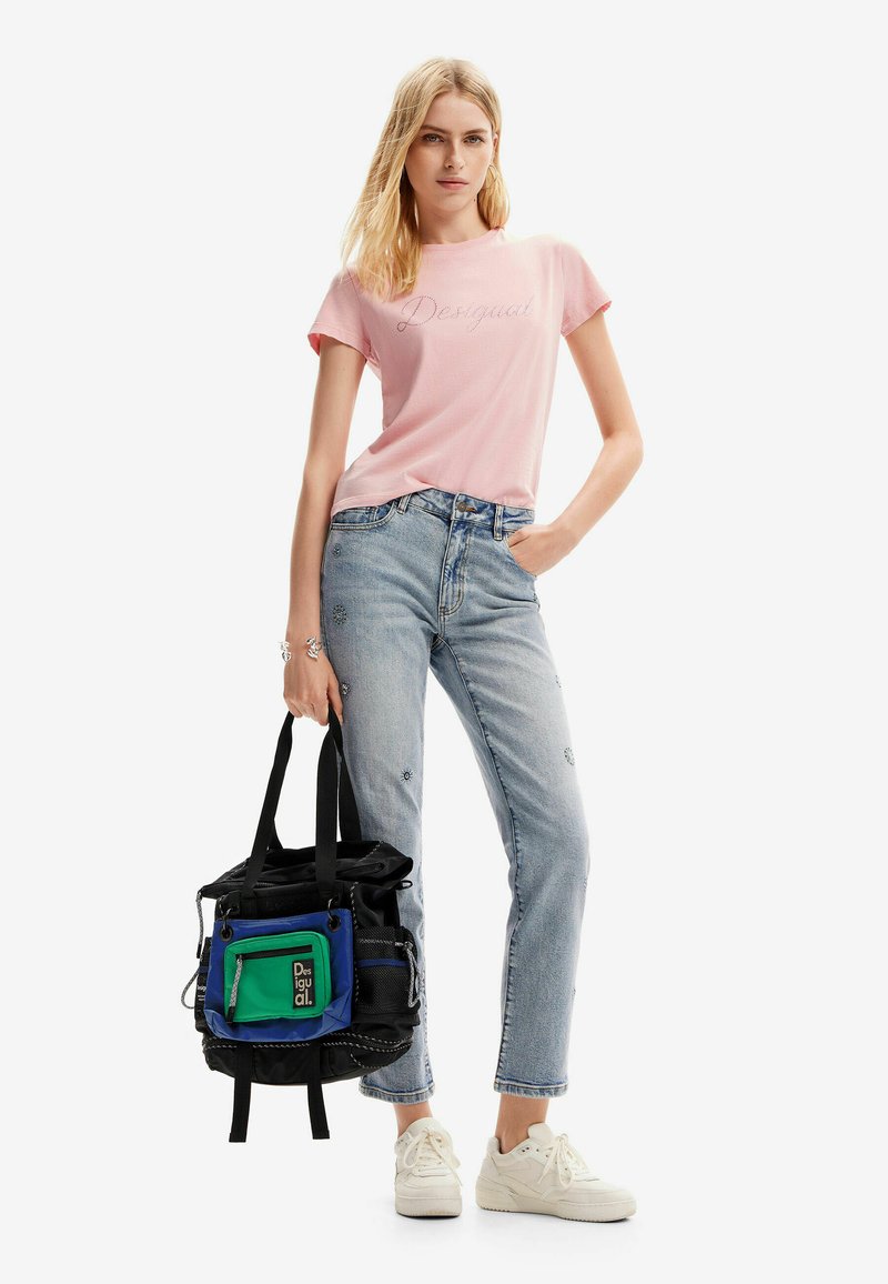 Light pink t-shirt with "Desigual" text, paired with blue jeans featuring floral embroidery, and a black multi-pocket bag with colored accents.