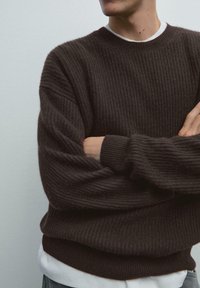 Bruine geribbelde breisweater met een ronde hals en een losse fit. Gelaagd over een witte shirt. Textuur, warme stof met lange mouwen.