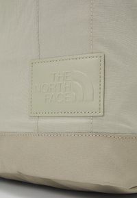 Tissu beige clair avec un patch cousu embossé du logo "THE NORTH FACE" sur un fond texturé.