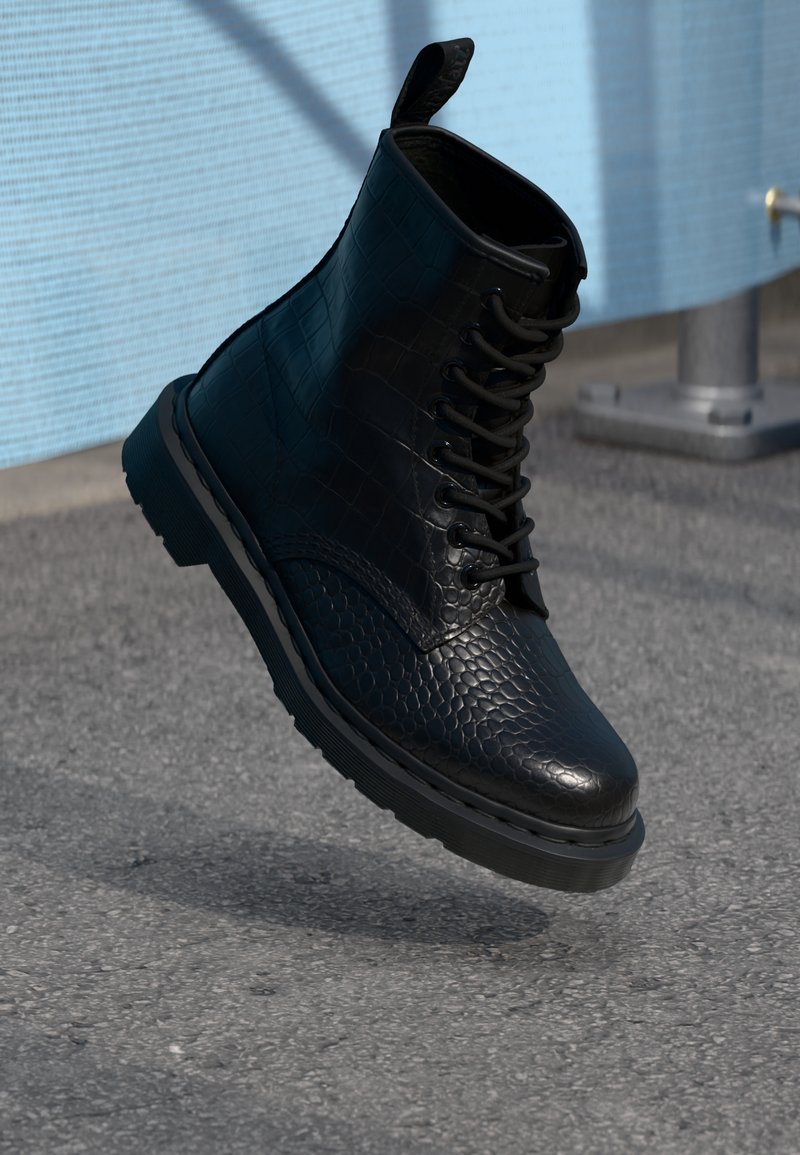 Botte noire en cuir texturé à lacets suspendue en l’air au-dessus d’une surface en asphalte proche d’un mur bleu clair et d’un poteau de rambarde métallique.