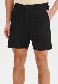 Czarne szorty wykonane z gładkiego materiału, z zapięciem na guzik, kieszeniami z przodu i prostym krojem, kończącym się powyżej kolana.