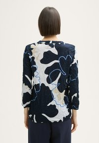 T-shirt à manches longues présentant une texture froissée avec des motifs floraux navy, blanc et beige, rehaussés de contours bleus. Encolure arrondie et coupe décontractée.