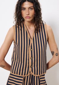 Gestreifter ärmelloser Pullover aus Baumwolle in Beige und Marineblau, mit V-Ausschnitt, vier Knöpfen und abgerundetem Saum mit passendem Streifenakzent.