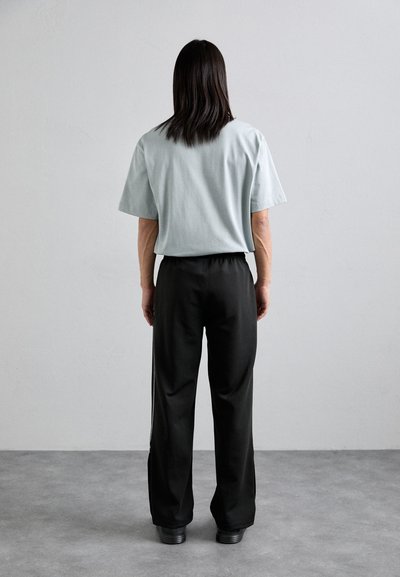 Chemise légère bleu clair à manches courtes associée à un pantalon noir à taille élastique, tous deux en tissu doux. Le pantalon a une coupe droite.