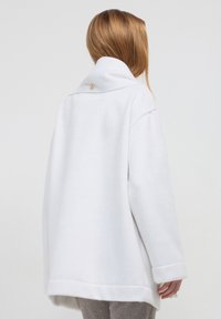 Cappotto bianco oversize con colletto alto e chiusura a bottoni sul retro. Tessuto morbido, design minimalista e senza motivi visibili.