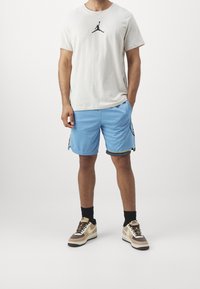 Camiseta gris claro con logo negro, pantalones cortos azules con bolsillos laterales y ribete negro, y zapatillas marrones con suelas blancas y cordones negros.