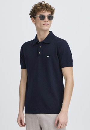 Marineblå polo skjorte laget av strikket stoff, med klassisk krage, tre-knapps placket og en liten logo på brystet. Korte ermer.