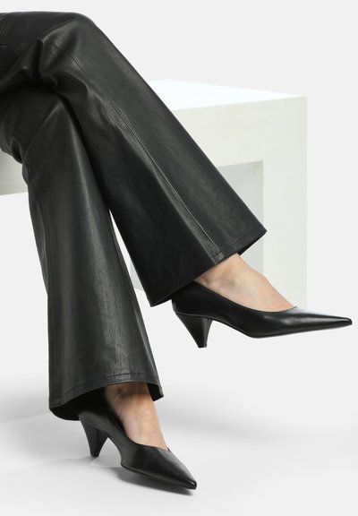 Melnas ādas augstpapēžu kurpes ar norādītu purngalu un konusveida papēdi. Gluda tekstūra, minimālisma dizains, komplektēts ar melnām biksēm.