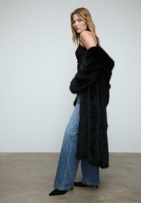 Svart fuskpäls lång kappa med en mjuk textur, ihop med ljusblå vida jeans med en diamantmönster och pärlaccenter.