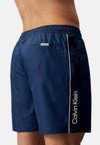 Shorts da nuoto navy con cintura elastica. Presentano una striscia laterale bianca e logo, una tasca sul retro e un tessuto liscio e leggero.