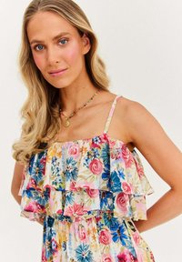 Kwiatowa sukienka z warstwowymi falbanami w pastelowych kolorach, z niebieskimi, różowymi i żółtymi kwiatami. Cienkie ramiączka i luźny krój.